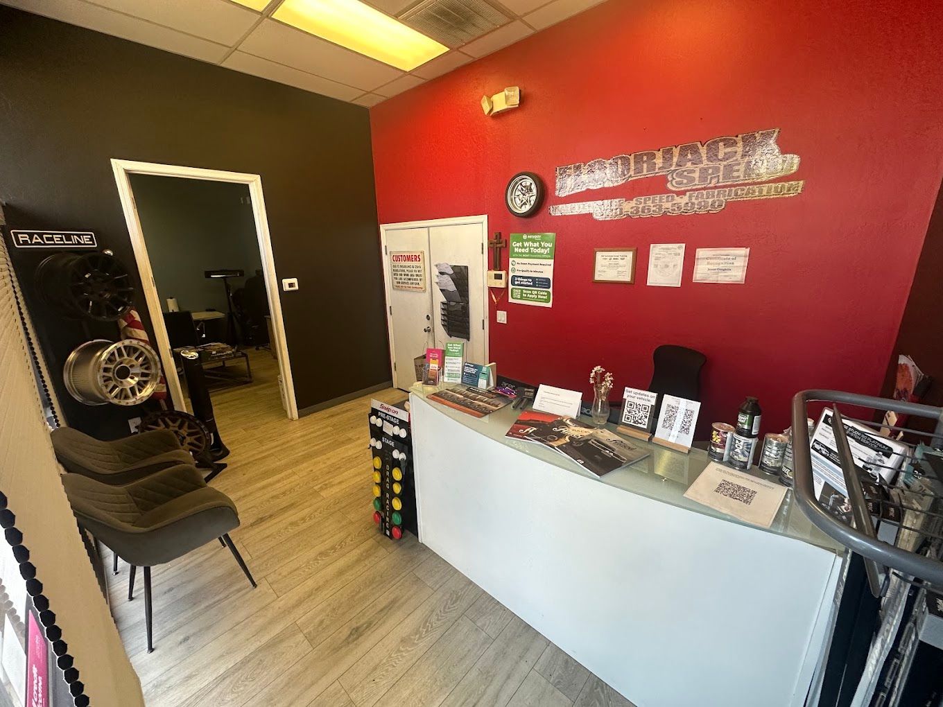 Inside the Floorjack Auto Repair front office in Phoenix — the customer counter beneath the red Floorjack Speed wall sign, with a wheel display and waiting-area seating