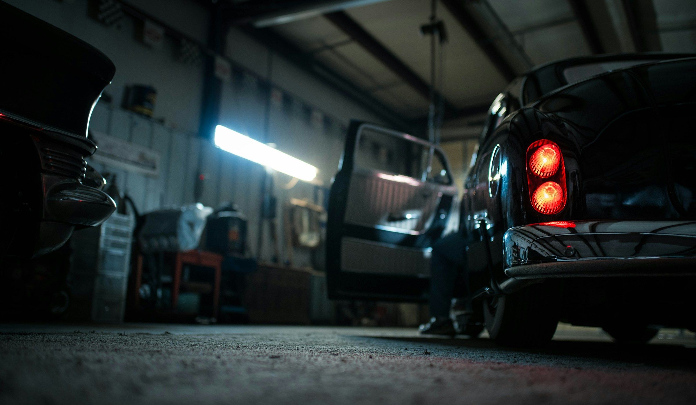 Inside the Floorjack Auto Repair service bay at night, a vehicle’s red taillight glowing in the dark shop