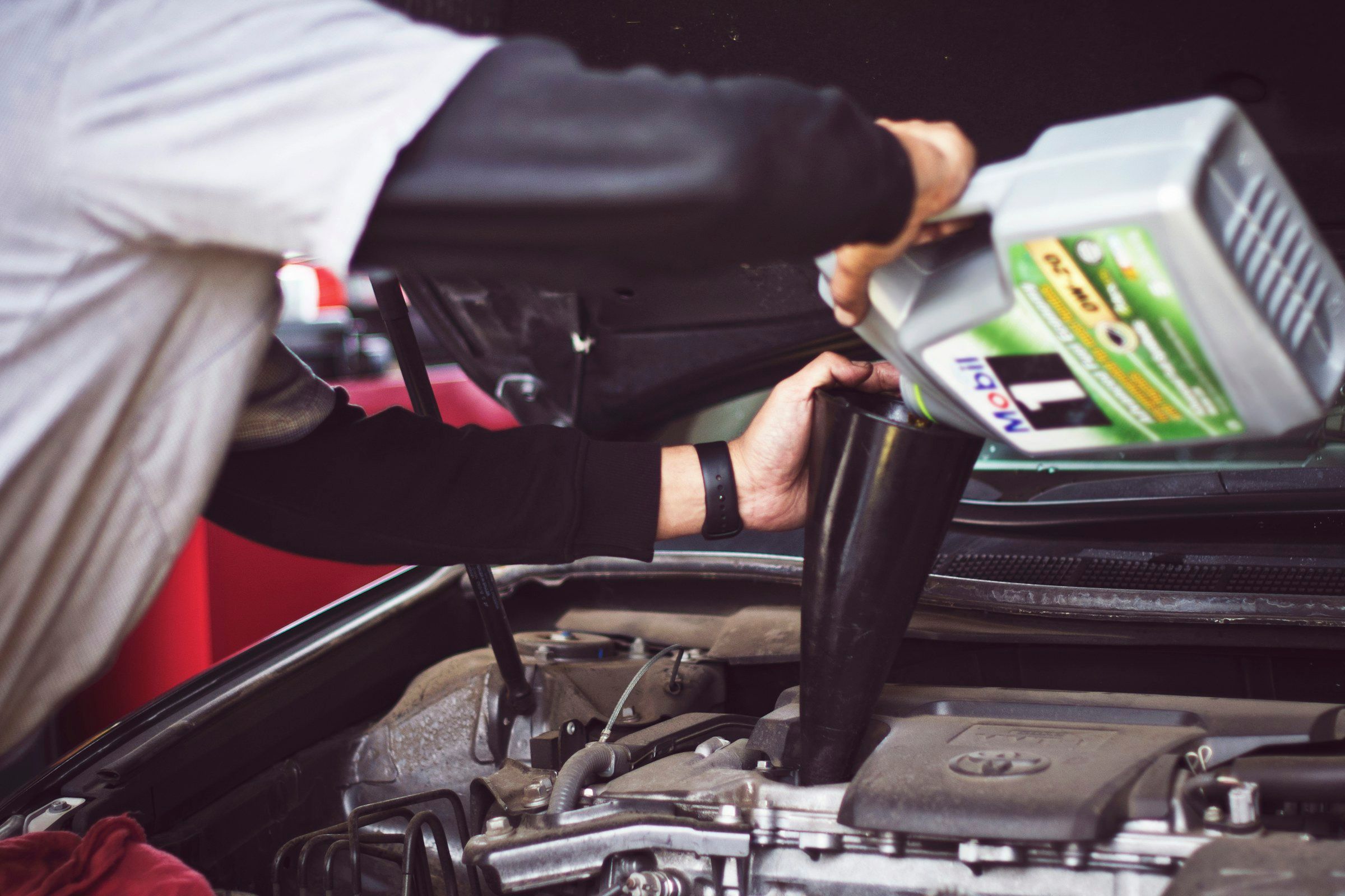 A technician pouring fresh motor oil into a car engine during an oil change